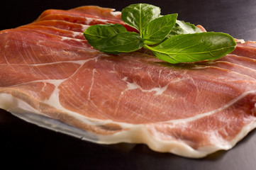 Prosciutto. Smoked pork rashers with basil on black background