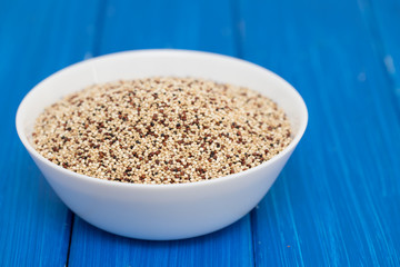 uncooked quinoa in white bowl on wooden background