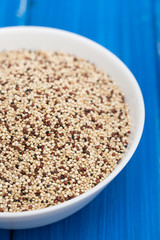 uncooked quinoa in white bowl on wooden background