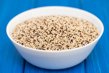 uncooked quinoa in white bowl on wooden background