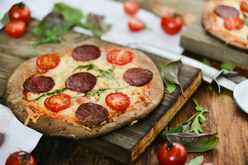 Mini Pizza With Cherry Tomatoes And Salami Sausages On A Wooden Background Natural Rustic, A Pizza Cutter And Ingridienty.