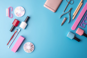 A set of cosmetic tools for manicure and pedicure on a blue background. Gel polishes, nail files and clippers, top view