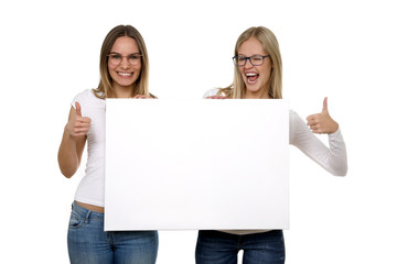 Zwei hübsche blonde Frauen mit Brille begeistert halten eine leere Tafel in  ihren Händen und Daumen hoch