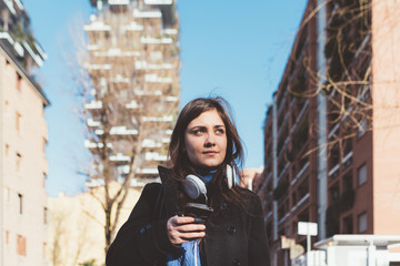 Portrait young woman outdoor back light looking away smiling headphones around neck - emancipation,...