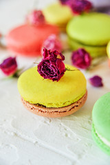 Dessert: A Delicate Fresh Colorful French Macaroons In Pastel Colors With Flowers Roses On A Light Textile Background, Top View