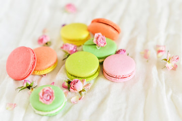 Delicate Fresh Colorful French Macaroons In Pastel Colors With Flowers Roses On A Light Textile Background, Top View