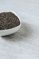 Vertical image of chia seeds in a white ceramic bowl on a wooden table.