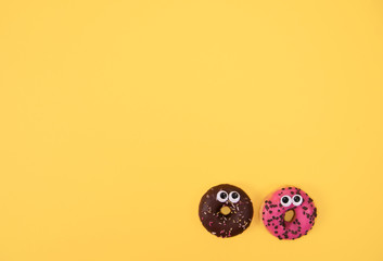 Colorful glazed donuts with funny eyes on yellow background.