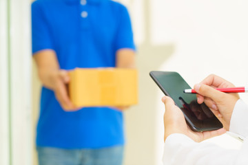 Woman receiving package and signing on digital mobile phone from delivery man