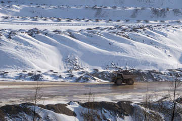 Loaded haul truck driving on a muddy road at an open pit mine in winter