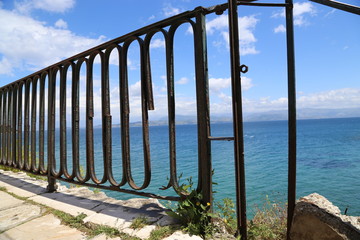 the sea is blue, the sky blue and blue with clouds in sunny day near port, Greece, Corfu through a metal fence