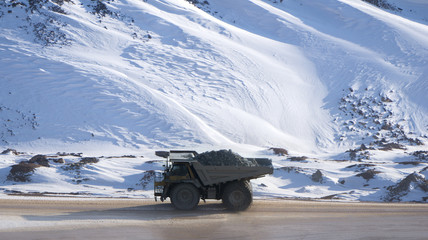Dump truck loaded with ore driving through a snow covered open pit mine