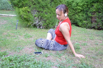 Fototapeta premium Young fitness woman in sportswear listening music with headphones after training outdoors at beautiful sunny day. Girl runner enjoying the sun and listen music in earphones from smartphone.