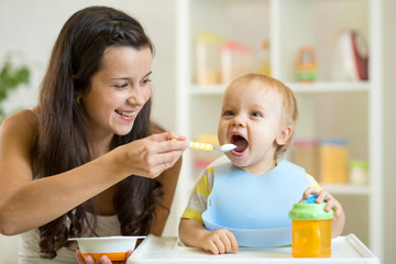 Mother feeding her baby with spoon. Mother giving healthy food to her adorable child at home