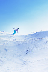 Naklejka na ściany i meble One snowboarder ride from a high snowy mountain under a blue sky.