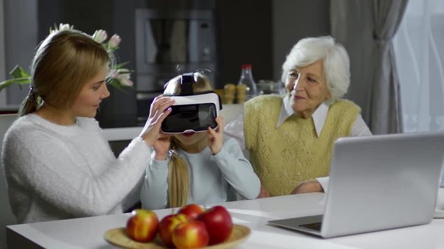 Little girl experiencing virtual reality with VR glasses while sitting at home with loving grandmother and beautiful mom
