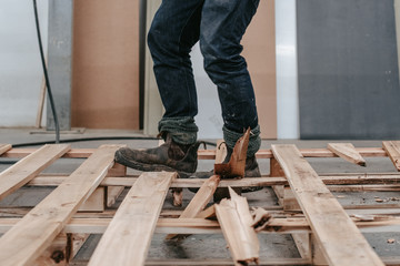 a craft worker man wearing boots in workshop trying to break a big wood into pices