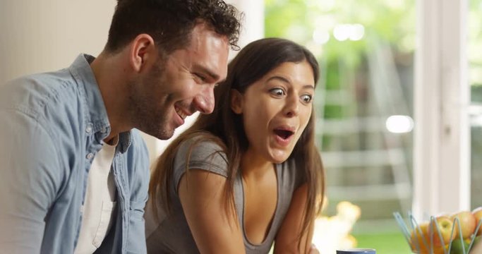 4K Happy couple browsing the internet at home, laughing at what they see on screen. Slow motion.