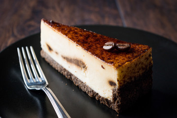 Coffee Cheesecake on Black Plate with Dark Wooden Surface.