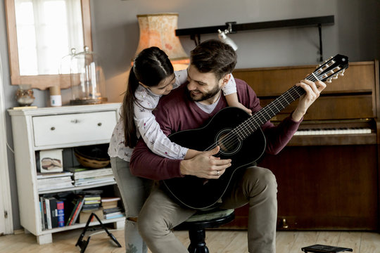 Man playing acoustic guitar for daughter in living room