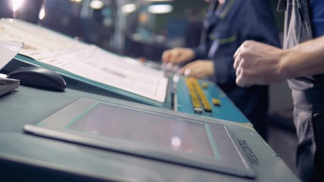 Male worker using digital computer touchscreen next to production line in factory.
