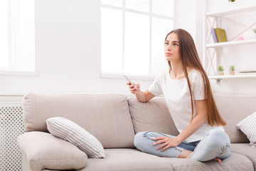 Pensive young woman sitting on sofa with cell phone