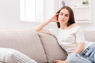 Young thoughtful woman sitting on sofa