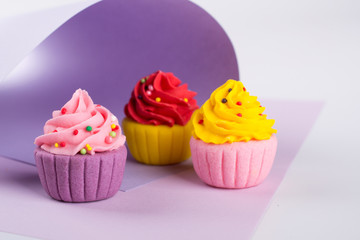 Decorative  multicolored sugar  cupcakes on light purple background with sprinkles