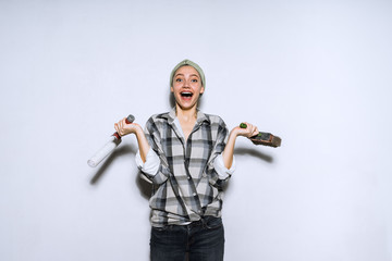 happy laughing young girl in plaid shirt holding roller and brush in hands for painting walls