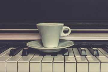 Cup of coffee on piano keys with copy space, concept of coffee break musical pause