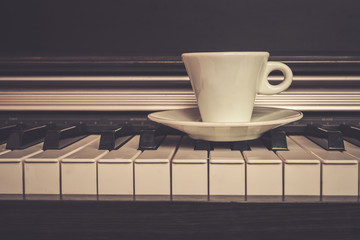 Cup of coffee on piano keys with copy space, concept of coffee break musical pause