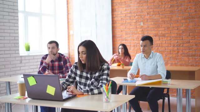 a group of young students sitting in the classroom and listening attentively to the teacher. University or school. A group of people mixed races. A girl invites classmates to look at information on