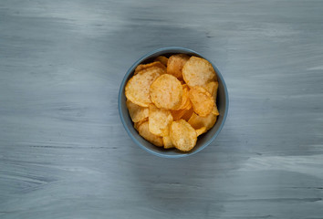 crisps in a blue bowl  on a light blue background, top view, space for text.Convenient snack concept