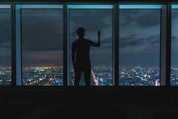 Fototapeta na wymiar Man writing on large windows high above a sprawling city at night