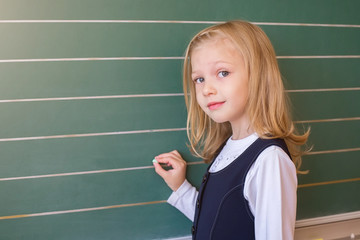 First grade pupil a girl writing on green blackboard at school lesson