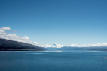 Obraz na płótnie Canvas Paisaje de picos de montañas nevados con cielo azul y nubes frente un lago y valle con árbol en el Monte Cook, Nueva Zelanda.