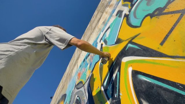 Graffiti artist is painting a yellow letter on the wall, view from below.