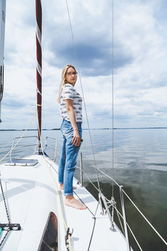 Slender barefoot blonde is standing on white yacht
