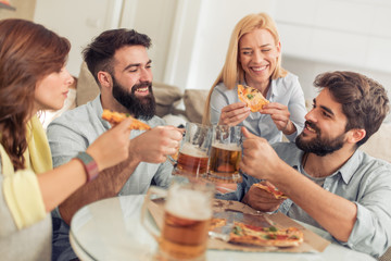 Happy friends eating pizza and watching tv at home