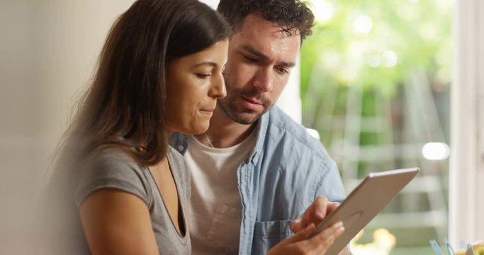 4K Happy attractive couple using computer tablet together at home. Slow motion.