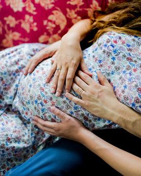 Detail og man and woman holding their hands upon 9 month pregnant belly