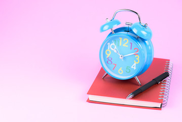 Blue retro alarm clock put on red book with black pen isolated in pink pastel background