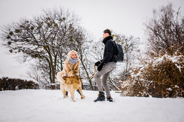 Fototapeta na wymiar A lovely couple plays with her dog in a snowy park