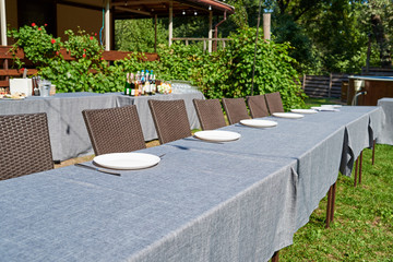 Dinner table with empty ceramic round plates and cutlery on grey tablecloth and chairs outdoors, copy space. Dinner plate setting. White plate with knife and fork
