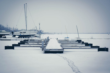 Sailboats moored in foggy harbor. Cold winter landscape with snow and ice