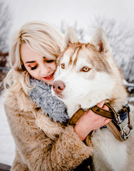 A abulous blonde hugs her dog in a winter park