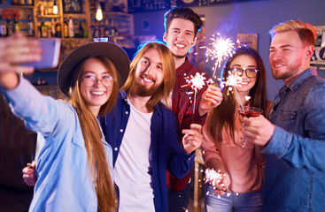 Selfie Time.Young Group of Friends Partying In A Nightclub And Toasting Drinks. Happy Young People With Sparklers At Pub. The People Have A Great Mood And They Smile A Lot.