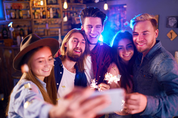 Selfie Time.Young Group of Friends Partying In A Nightclub And Toasting Drinks. Happy Young People With Sparklers At Pub. The People Have A Great Mood And They Smile A Lot.