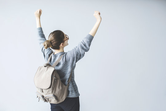 Confident young female student raised up arms with backpack