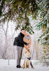 A lovely couple standing in a hug near a tree with their dog